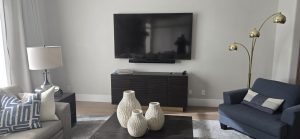 Modern living room with a television mounted on the wall, a stylish blue sofa, decorative vases on a coffee table, and a floor lamp, emphasizing contemporary interior design suitable for enhancing business environments.
