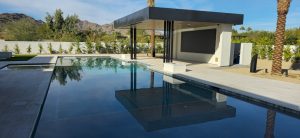 Modern poolside area with sleek design, featuring a glassy pool reflecting a contemporary structure and surrounding palm trees, emphasizing relaxation and luxury.