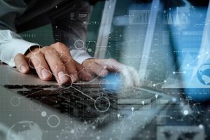 Person typing on laptop surrounded by digital data visualizations, representing Minding Your Media's IT services and solutions for business transformation.